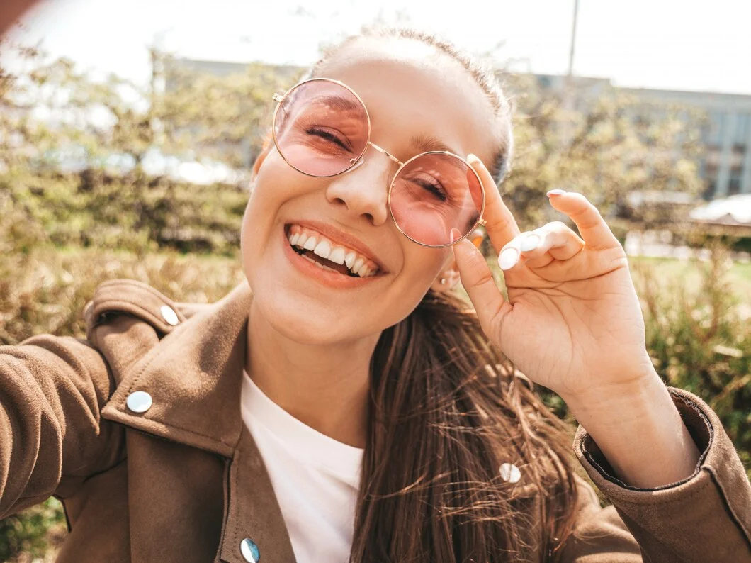 woman smiling and wearing pink, round sunglasses
