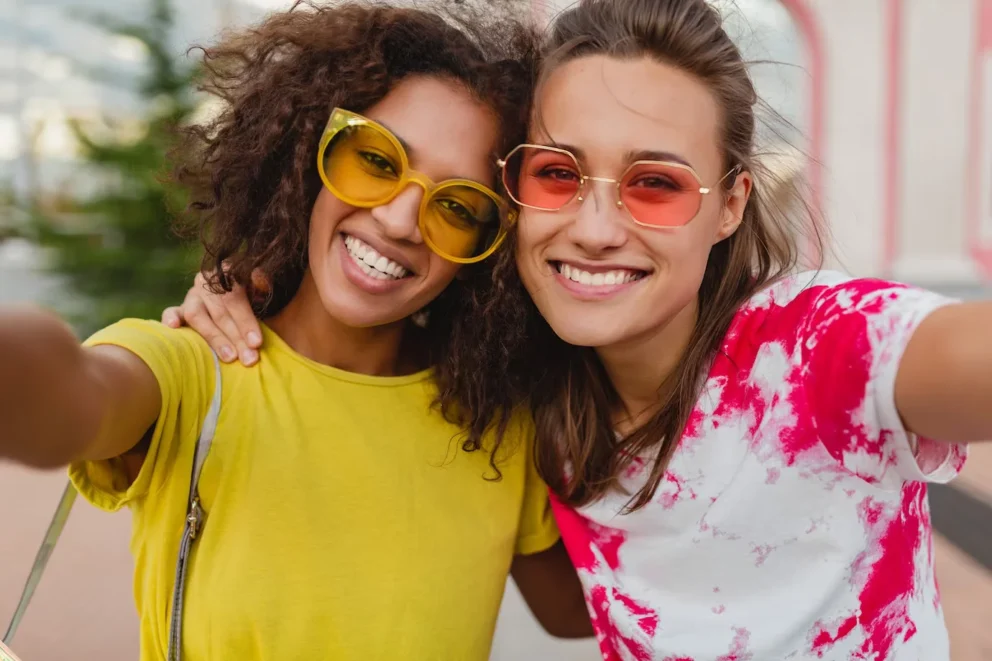 two girls in sunglasses hugging and smiling next to each other