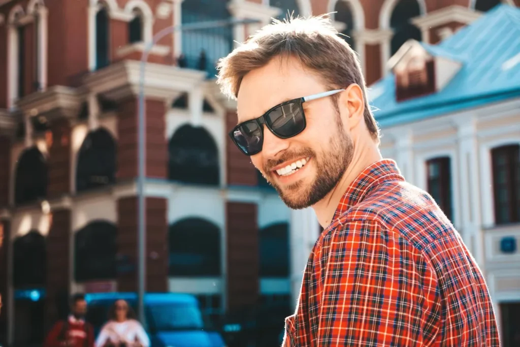 man smiling while wearing a plaid shirt and sunglasses outside of Manhattan dental clinic